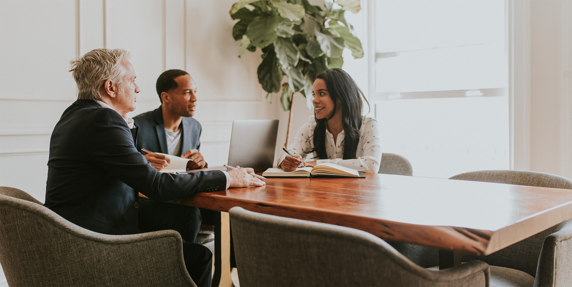 Kolme ihmistä tekemässä töitä pöydän ääressä toimistossa