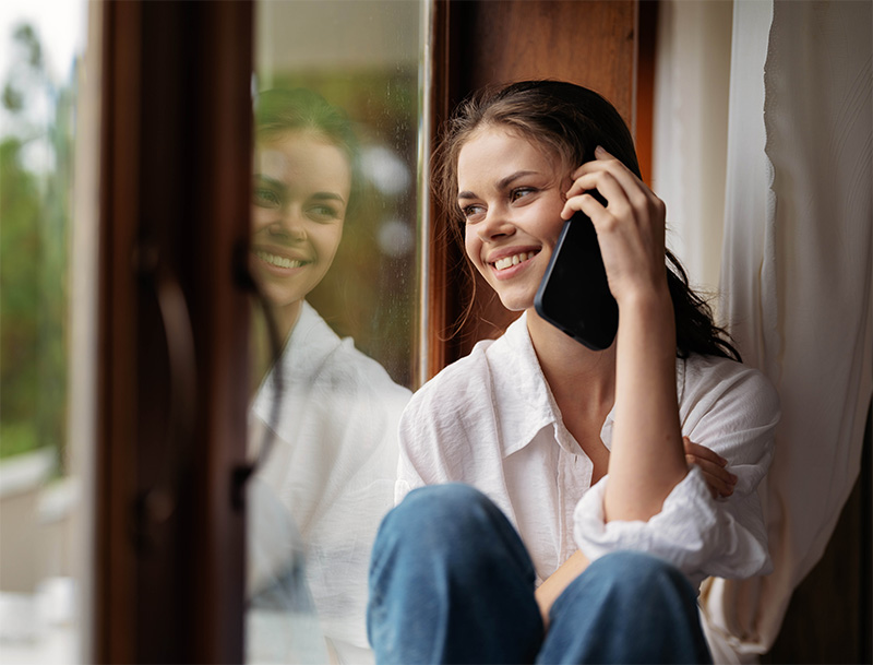 Nainen soittamassa puhelua kotona ikkunan ääressä